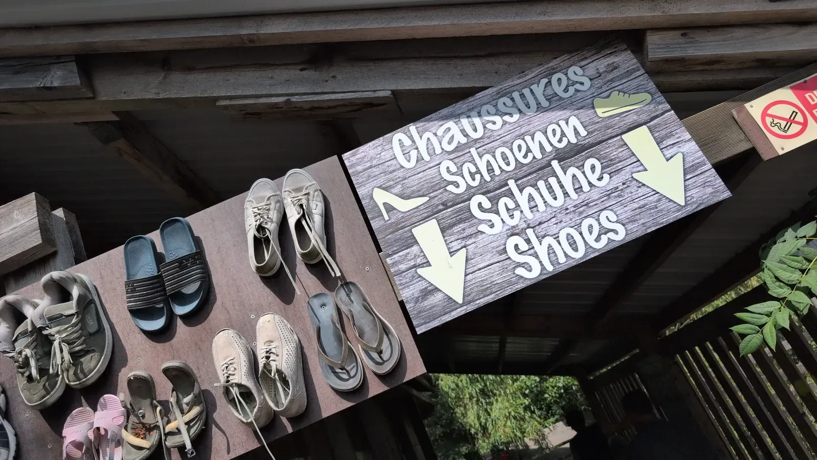 Meertalig bord dat vraagt om je schoenen uit te doen vóór het blootsvoetspad